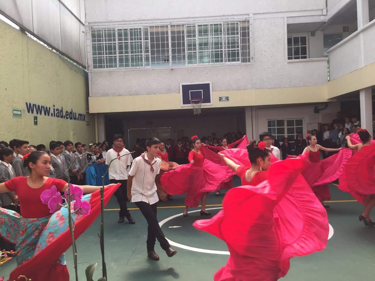 Parejas de alumnos bailan un baile folclórico en el patio mientras sus compañeros observan