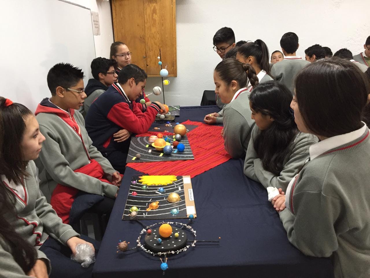 Alumnas y alumnos de secundaria alrededor de una mesa con maquetas del sistema solar