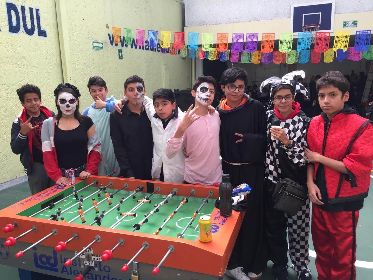 Alumnos disfrazados para Día de Muertos posan alrededor de un futbolito en el patio