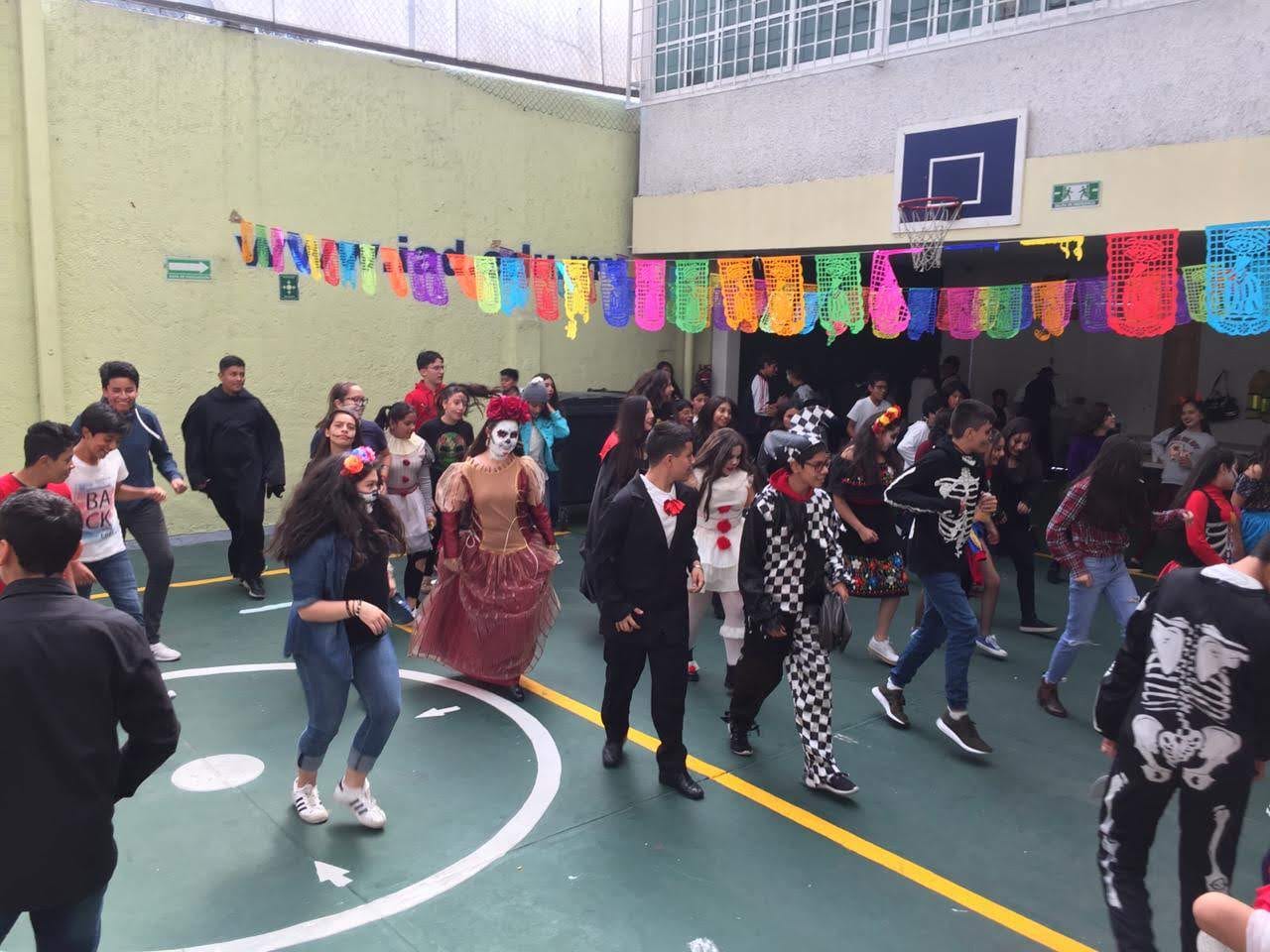 Alumnos disfrazados caminan y bailan en el patio durante la celebración de Día de Muertos