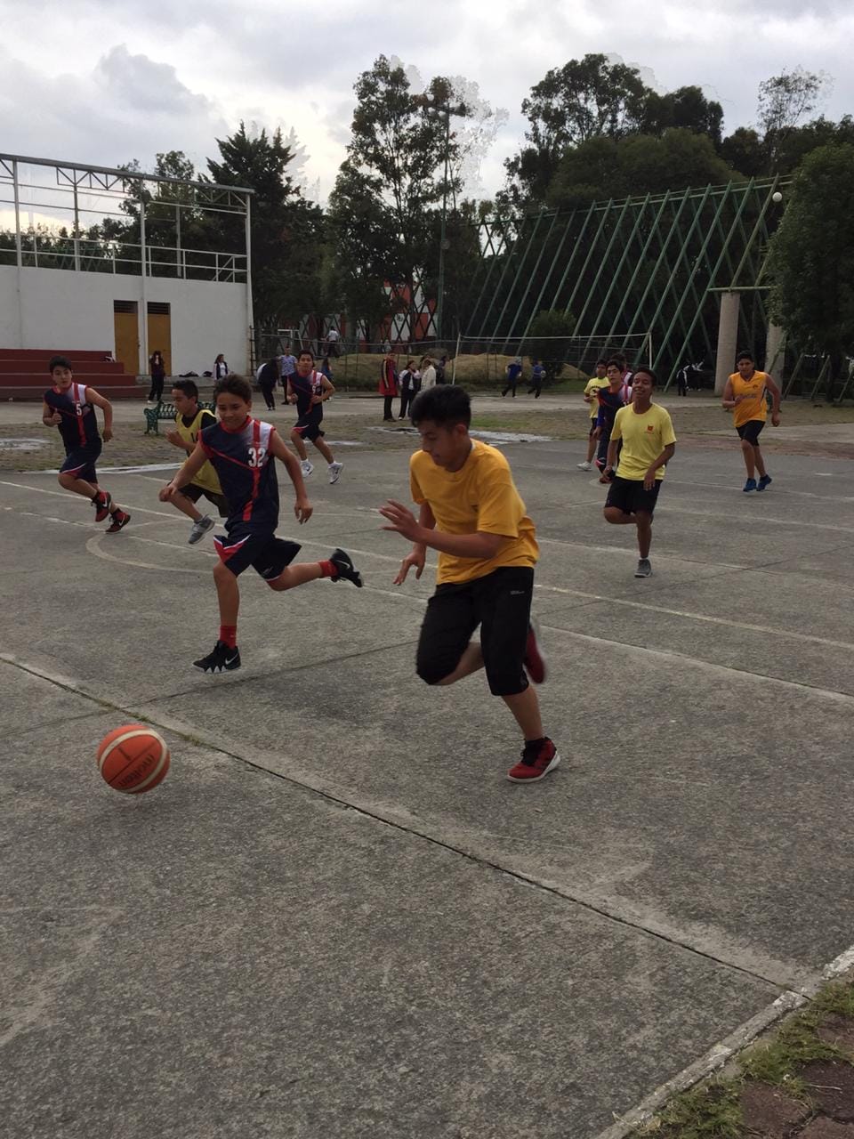 Alumnos de secundaria juegan un partido de básquetbol en una cancha al aire libre