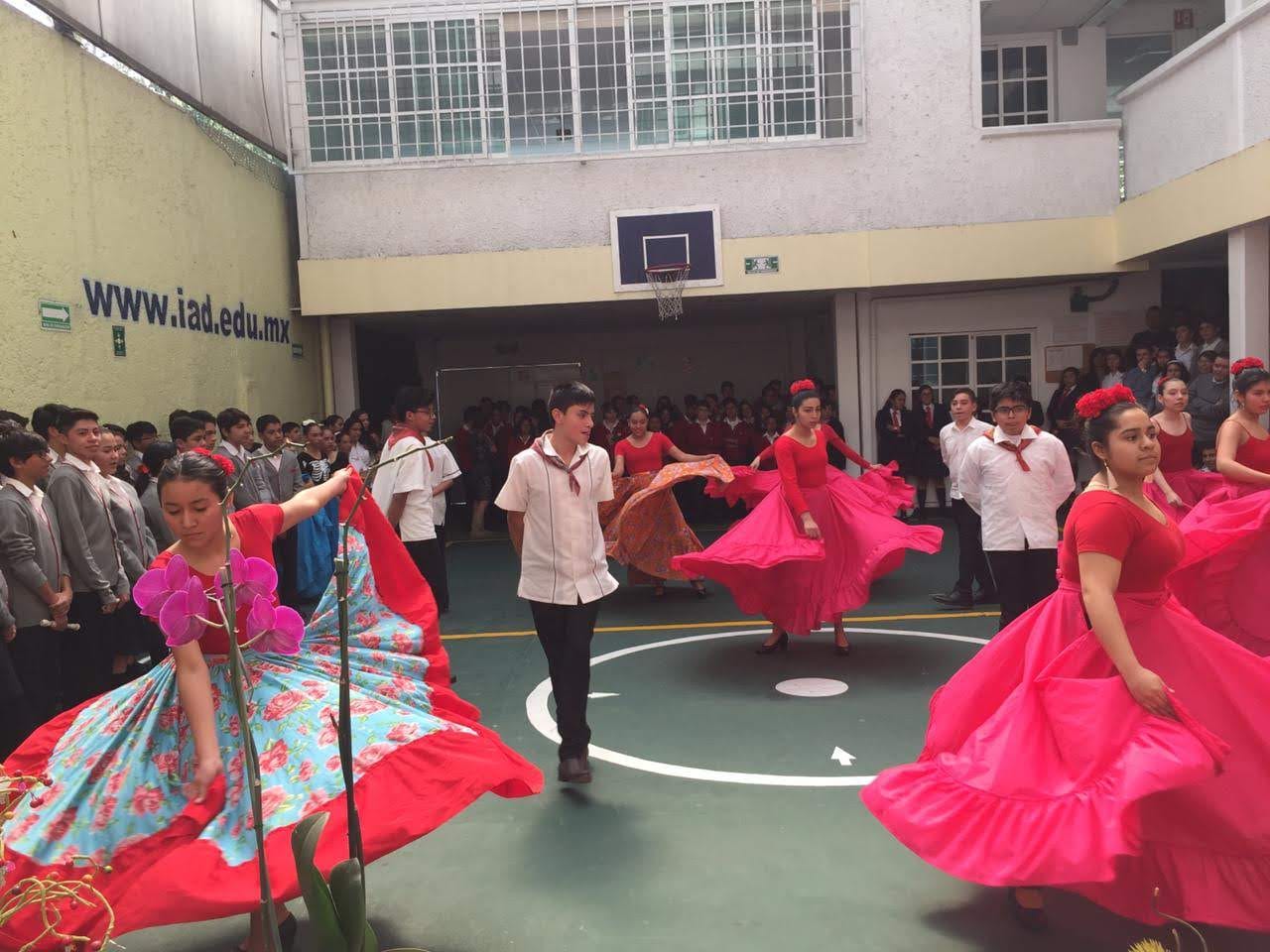 Alumnas y alumnos bailan un baile folclórico con faldas rojas en el patio del plantel