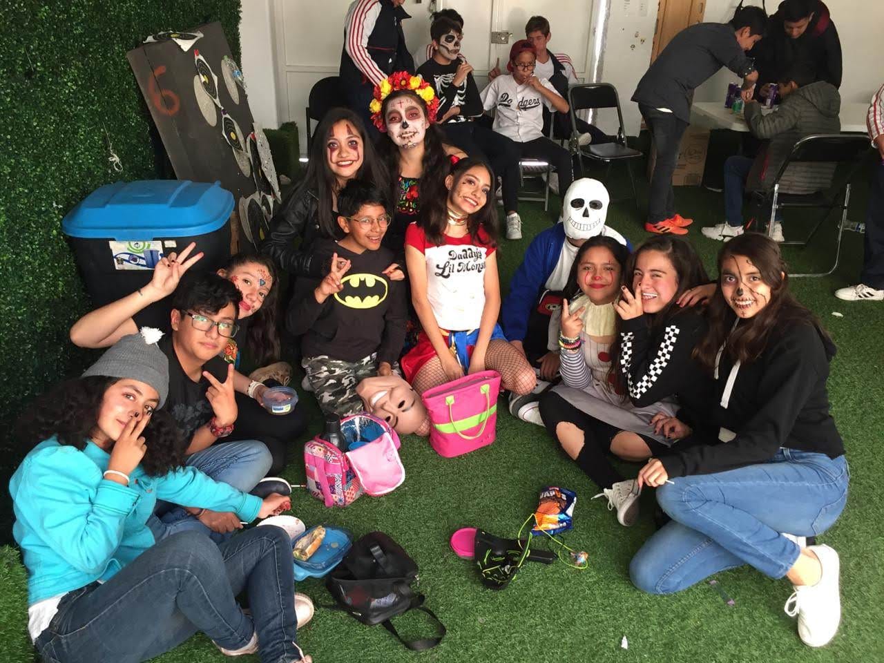 Un grupo de alumnas y alumnos con maquillaje de Día de Muertos convive sentado en el pasto